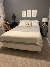 Neatly made bedroom with a bed, three wall art panels, and a lamp on a gray wall.
