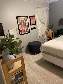 Neat bedroom with a bed, framed wall art, window, chair, plant, and small ottoman.