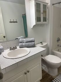 Small bathroom with white vanity, round sink, wall cabinet, towel rack, and toilet beside a tub.