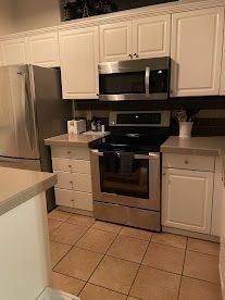 Modern kitchen with stainless steel appliances, white cabinets, and tan tile floor.