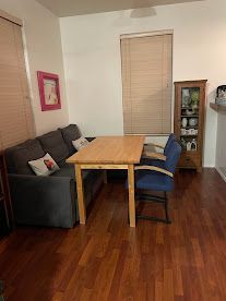 Dining area with wood table, gray sofa, blue chairs, and a glass cabinet on hardwood floor.