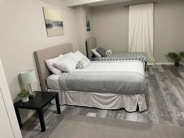 Bedroom with two neatly made beds, a nightstand, wall art, and a window with curtains.