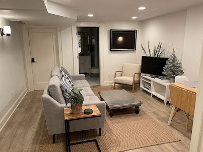 Cozy living room with gray sofa, ottoman, TV console, armchair, and woven rug in a modern neutral interior