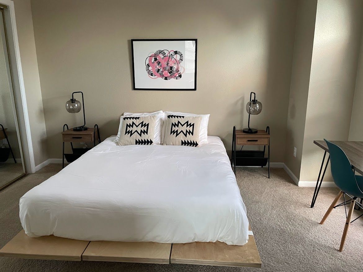 Minimal bedroom with a white bed, nightstands, lamps, and framed art above the headboard.