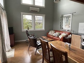 Bright living room with red sofa, wooden chairs, large windows, and a dining table under a mirror.