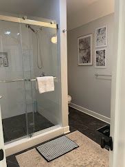 Modern bathroom with glass shower, towel, framed wall art, and dark tiled floor.