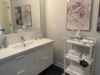 Modern bathroom vanity with mirror, sink, floral wall art, and a white shelving cart with towels and decor