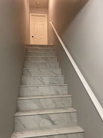 Narrow staircase with white banister leading to a closed white door at the top.
