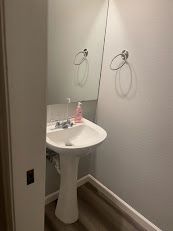 Small bathroom with a white pedestal sink, mirror, and two wall-mounted towel rings.