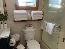 Small bathroom with toilet, towel rack, sink, and glass shower door, neatly stocked with rolled towels.