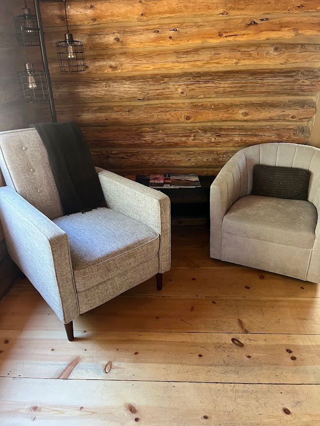Two beige armchairs with dark cushions beside a rustic wooden wall and floor