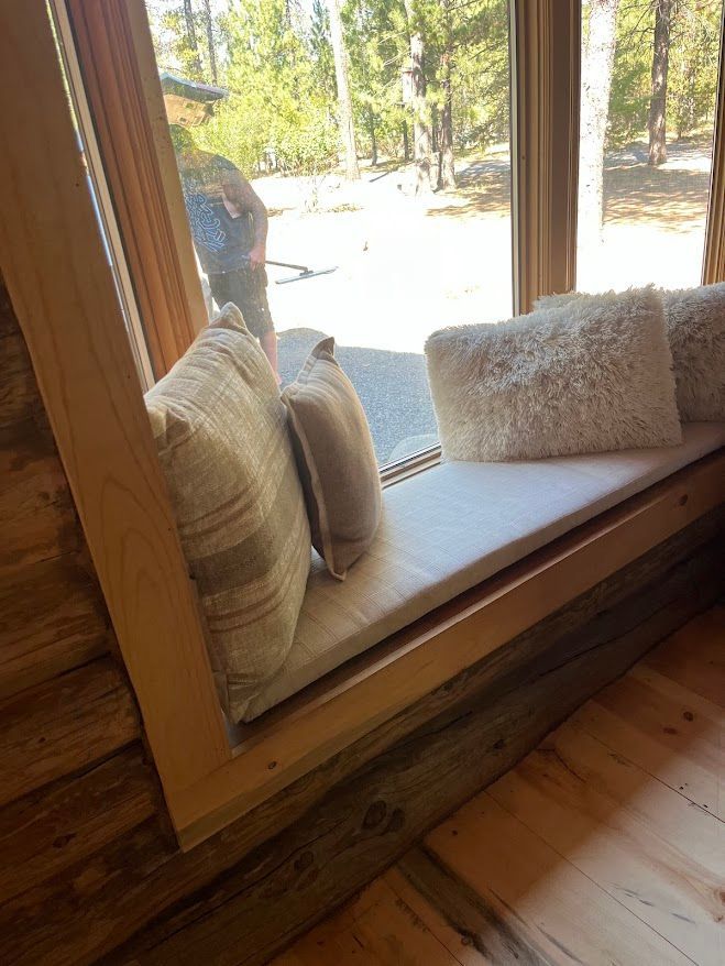 Wooden window seat with beige pillows overlooking a bright wooded outdoor scene