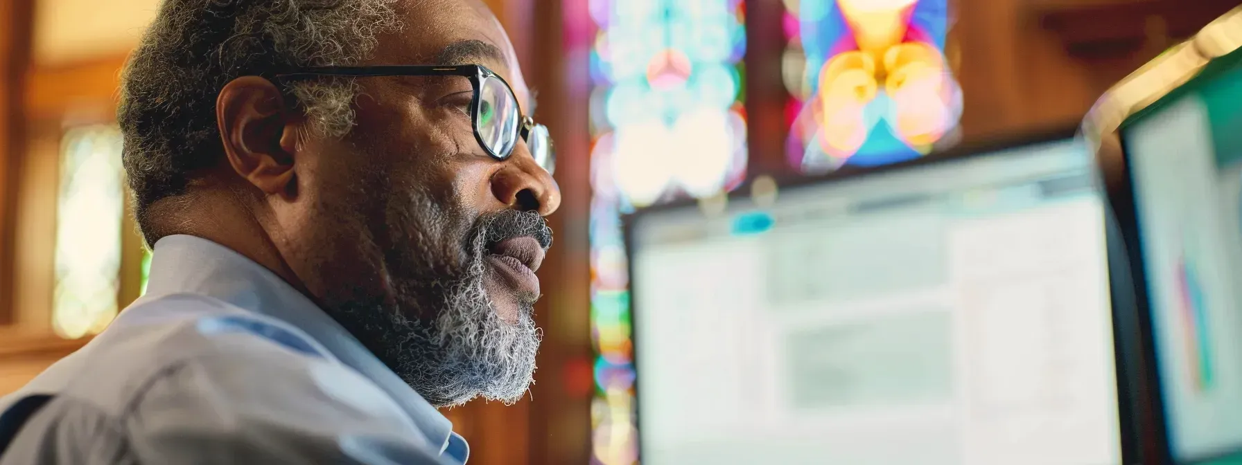 A man with glasses is sitting in front of a computer in a church.