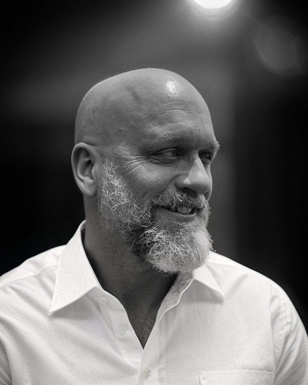 Black-and-white portrait of a smiling bald man with a beard in a white shirt, looking to the side