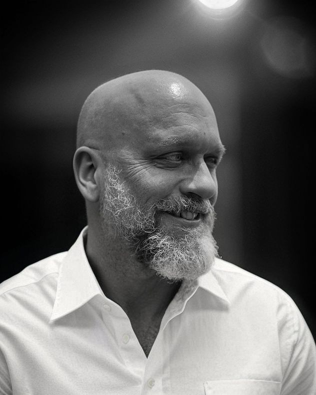 Black-and-white portrait of a smiling bald man with a beard in a white shirt, looking to the side