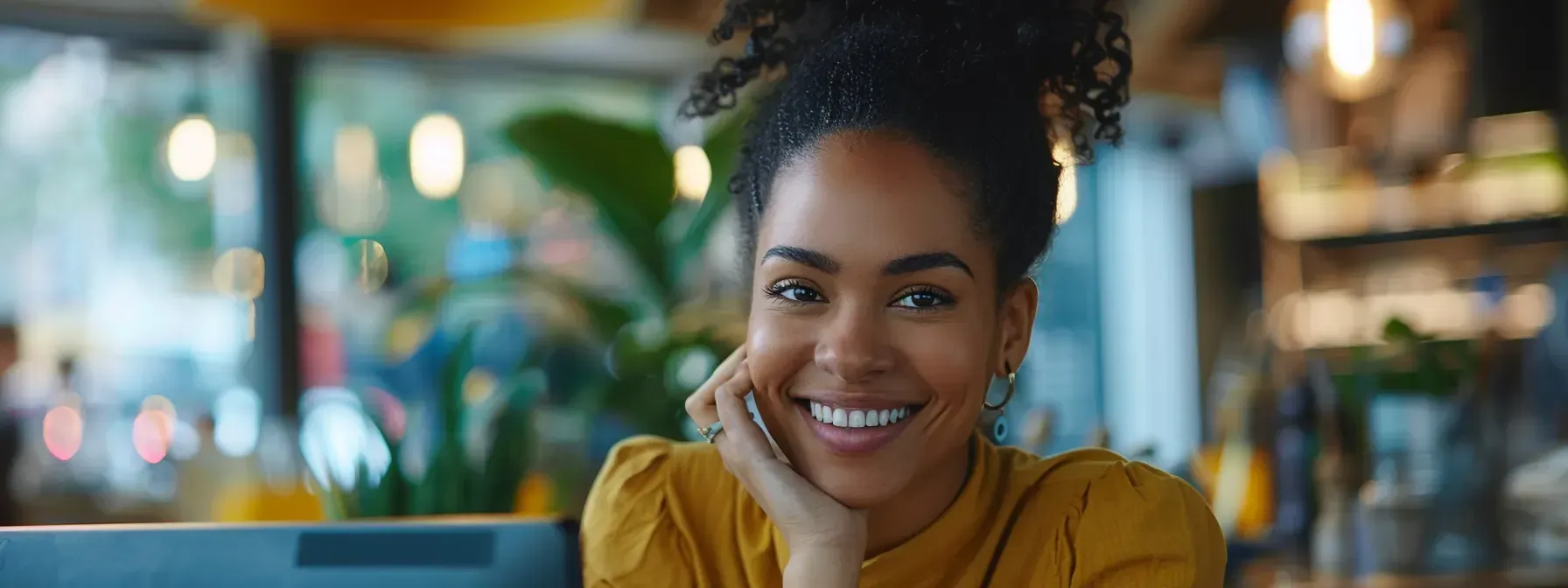 A woman is smiling while sitting at a table in front of a laptop computer.