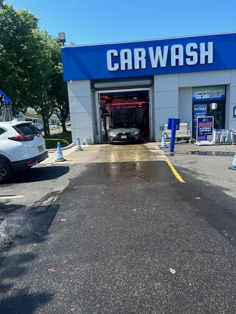 A car drives into a blue-and-white automated car wash facility on a sunny day.