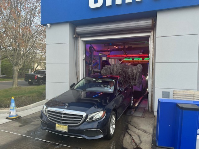 A dark blue Mercedes-Benz convertible entering a car wash bay with red neon lighting visible inside.