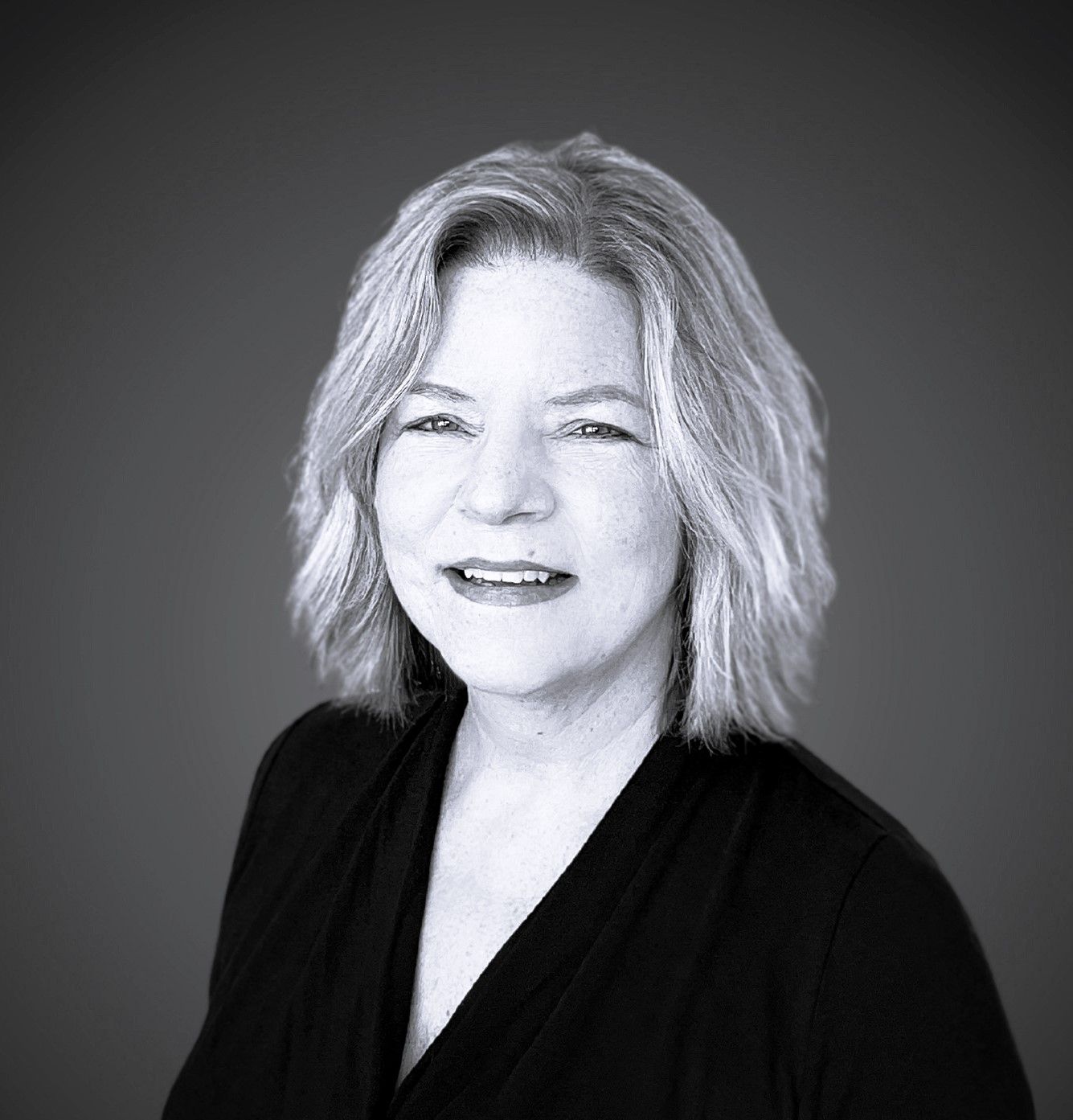 A Cynthia in a black shirt is smiling in a black and white photo.
