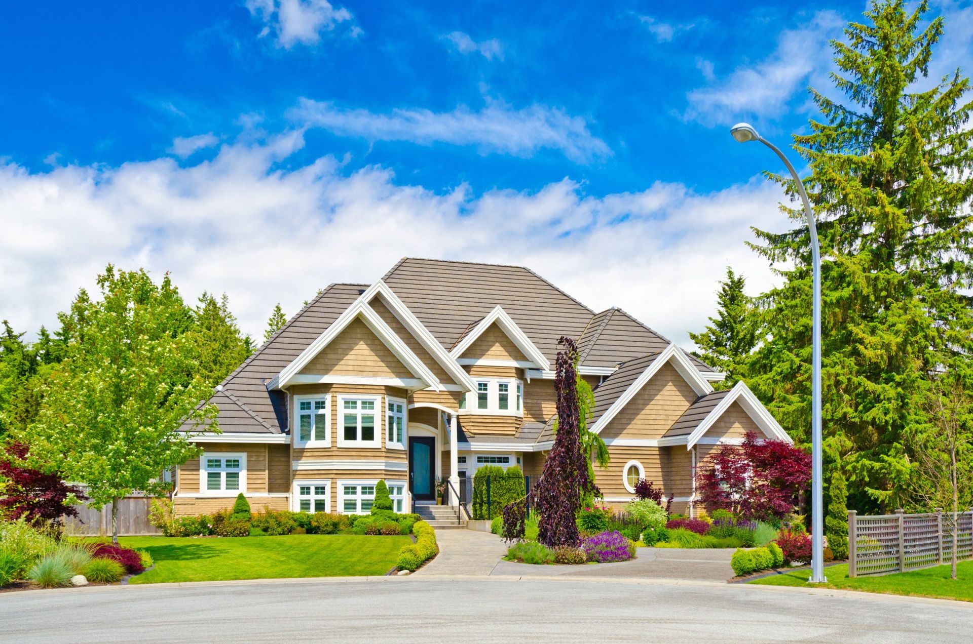 Large suburban house with a manicured lawn, driveway, and blue sky on a sunny day