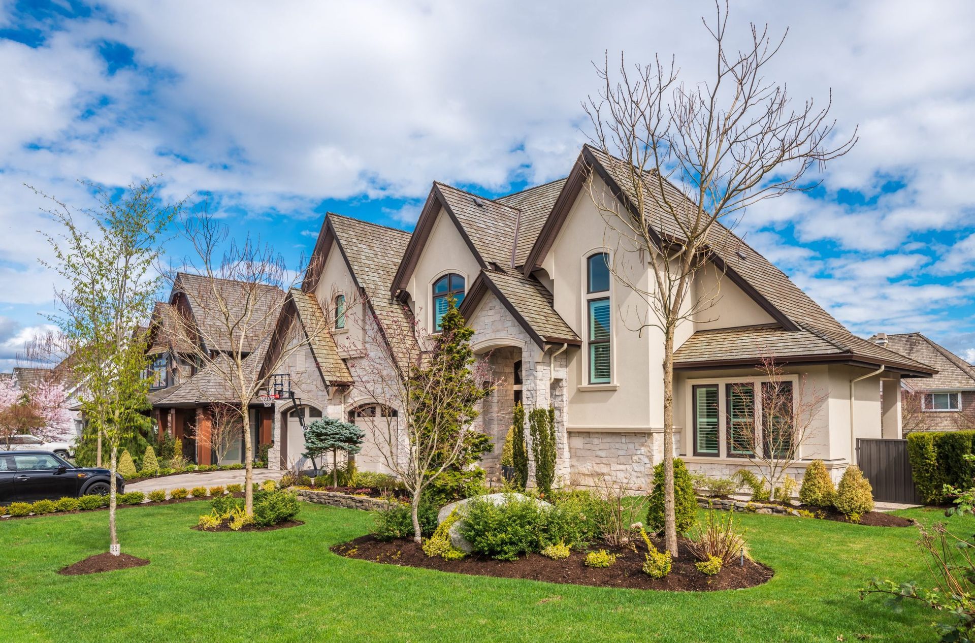 Row of modern suburban houses with manicured lawns and landscaped gardens under a partly cloudy sky