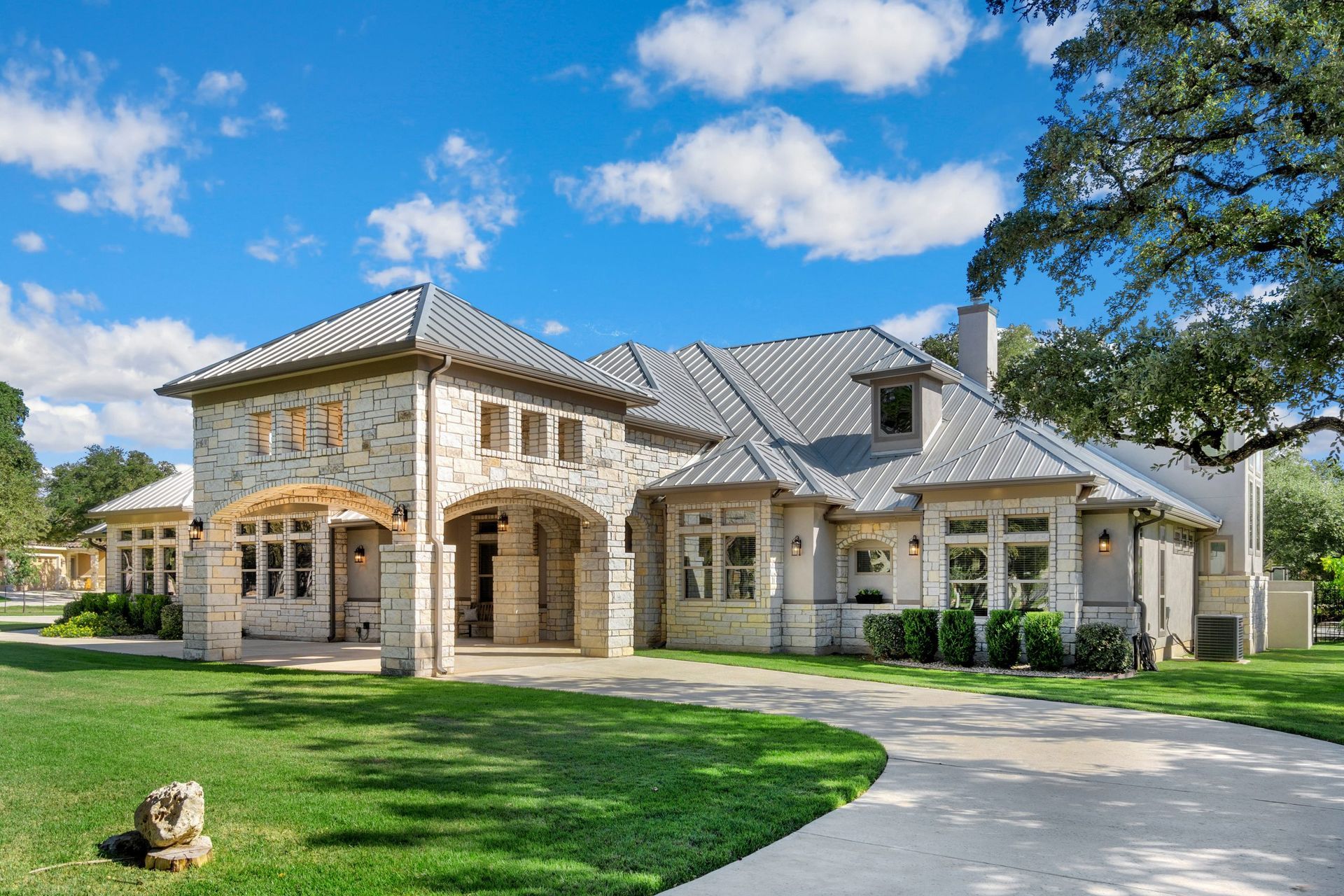 Large stone house with arched entry, gray roof, and green lawn under a blue sky