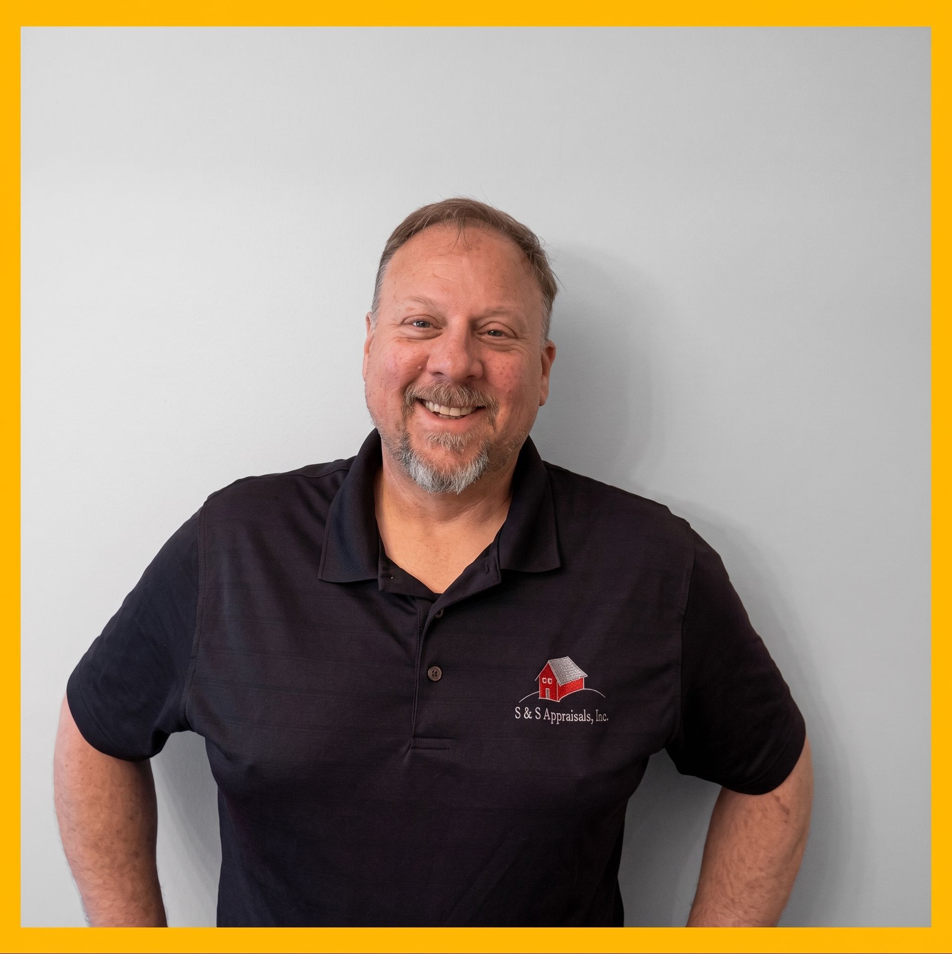 Smiling man in a black polo shirt standing against a plain white wall