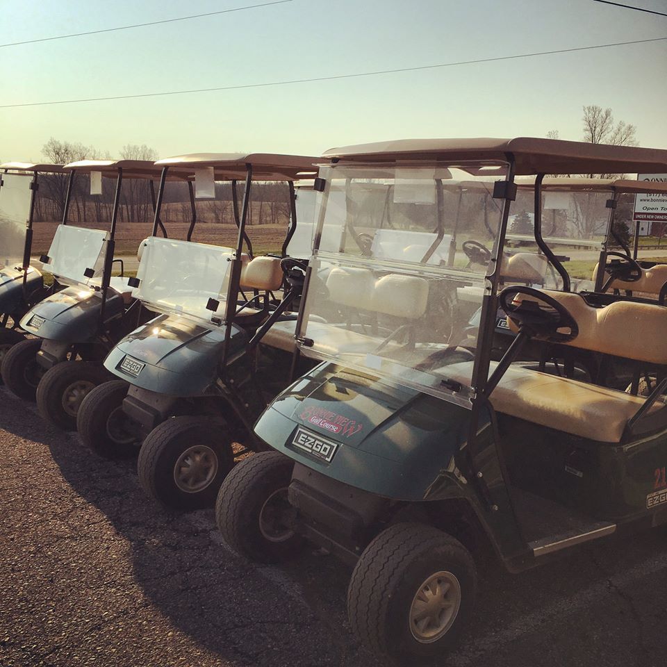 A row of golf carts are parked in a parking lot