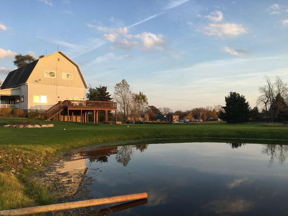 There is a barn in the background and a pond in the foreground.