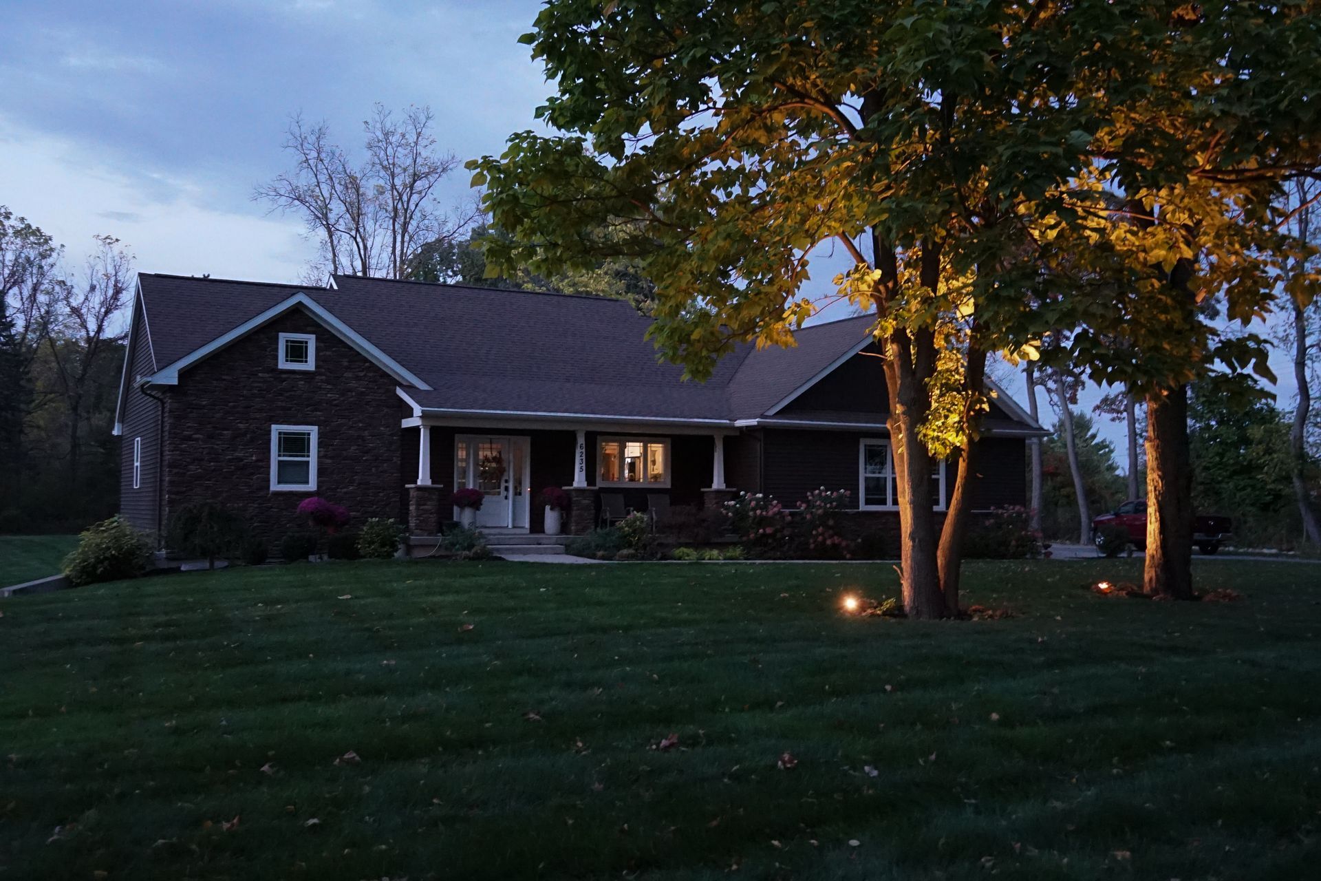 Brick house at dusk with lit porch and trees in the front yard