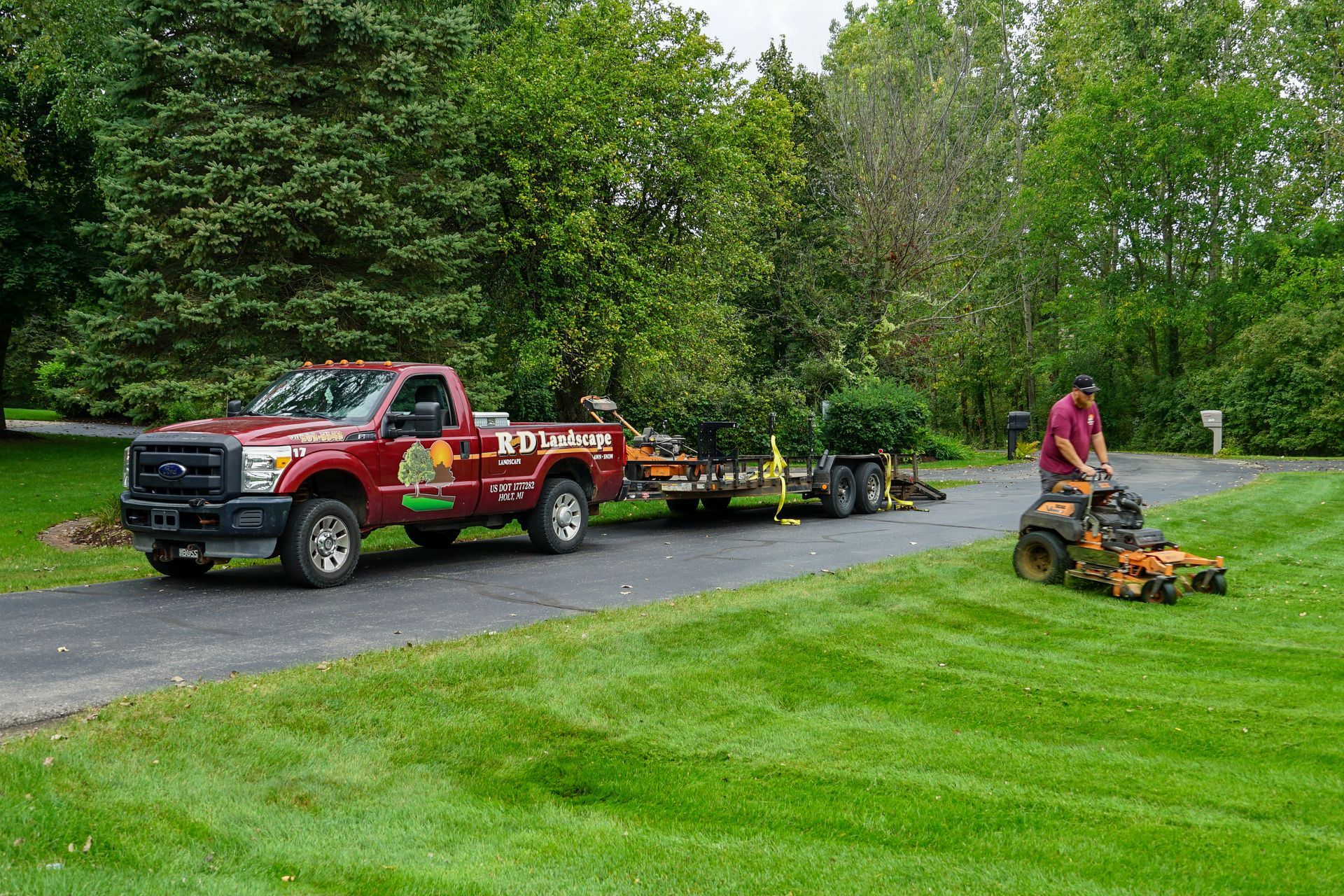 A man is mowing a lush green lawn next to a red truck.