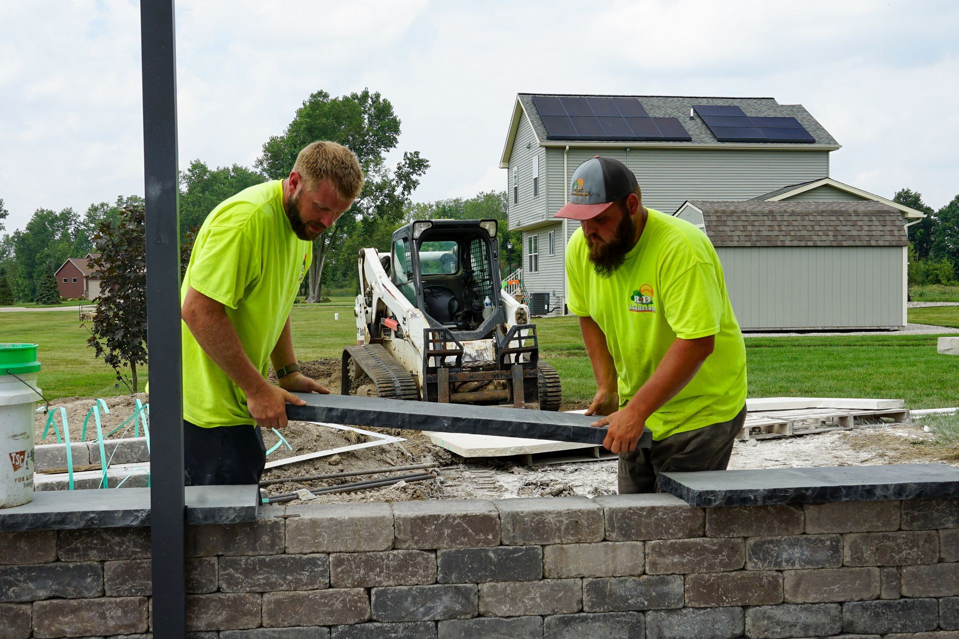 Two workers in neon shirts trowel mortar on a stone wall at a construction site