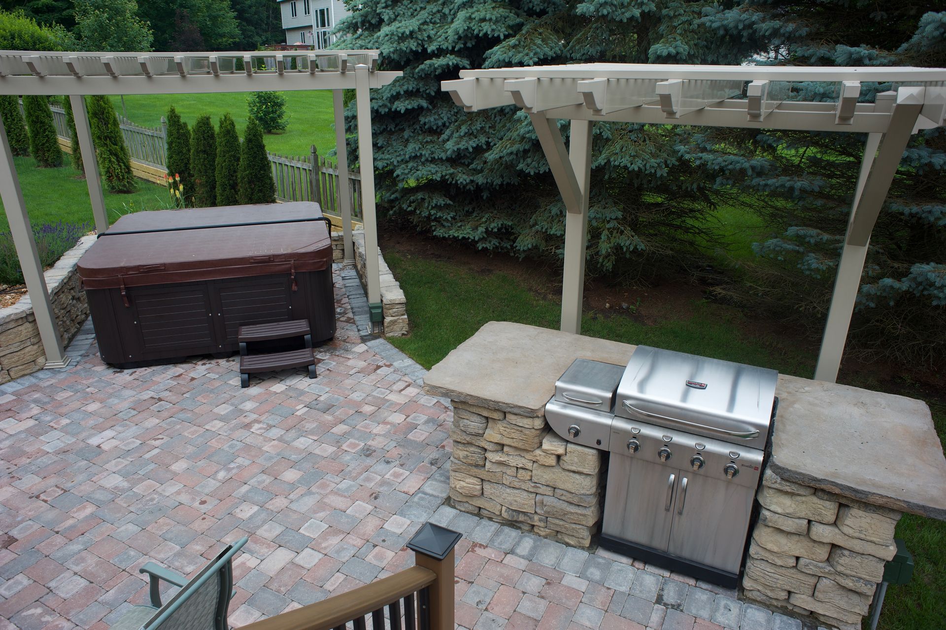 A patio with a grill and a hot tub under a pergola