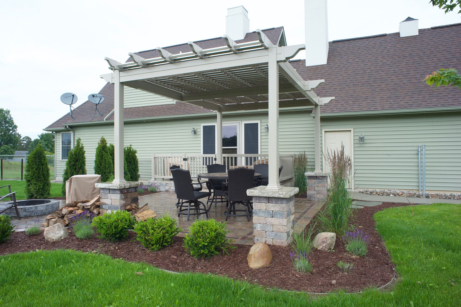 A patio with a table and chairs under a pergola in front of a house.