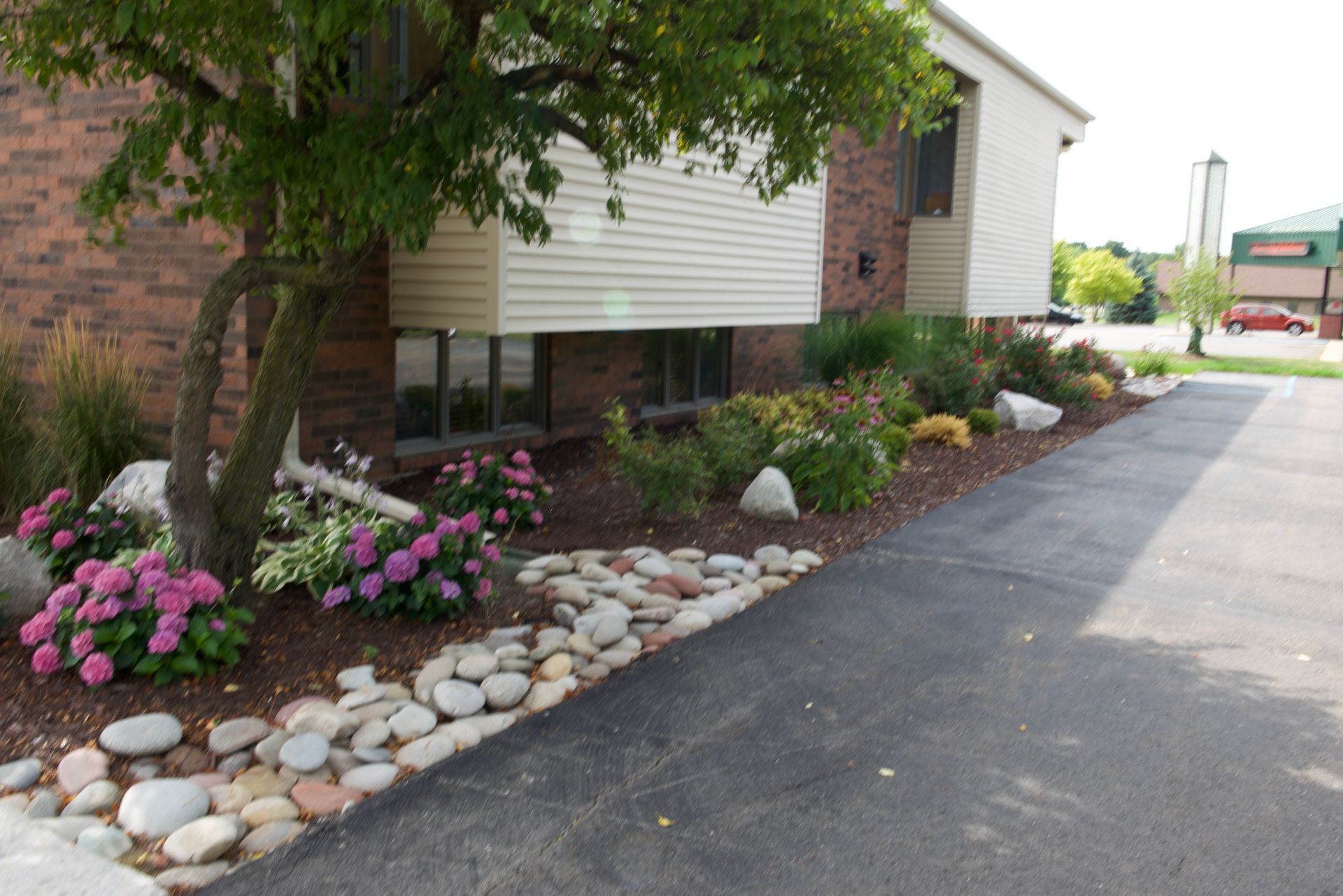 Landscaped building exterior with pink flowers, stone border, and paved driveway
