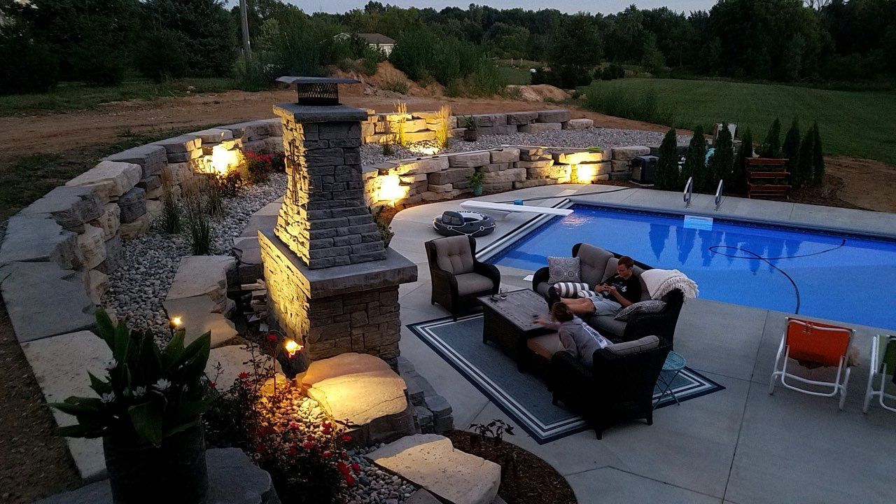 A patio area with a fireplace and a swimming pool in the background.