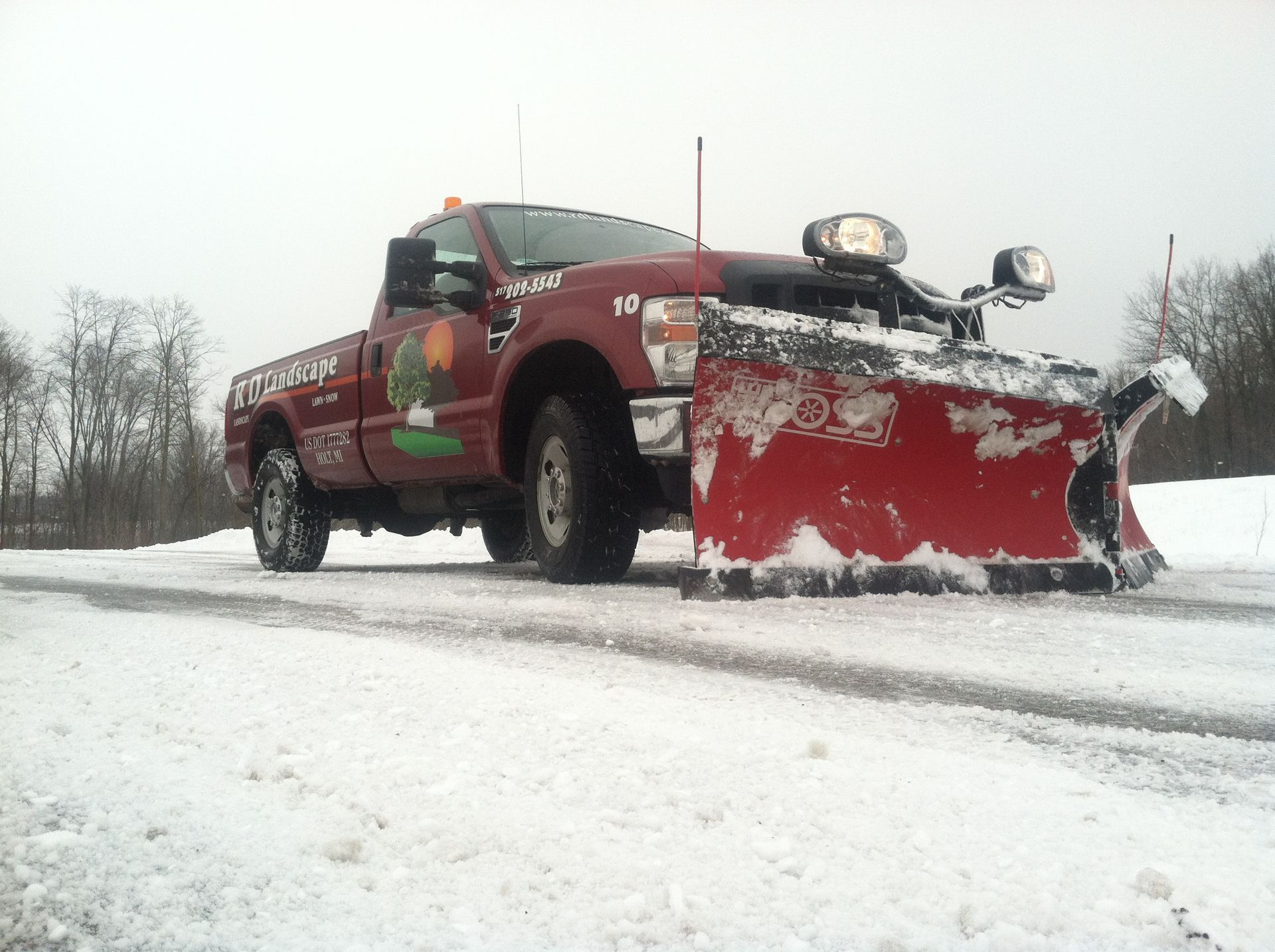 Red snowplow truck clearing a snowy road, front blade pushing snow on a winter day