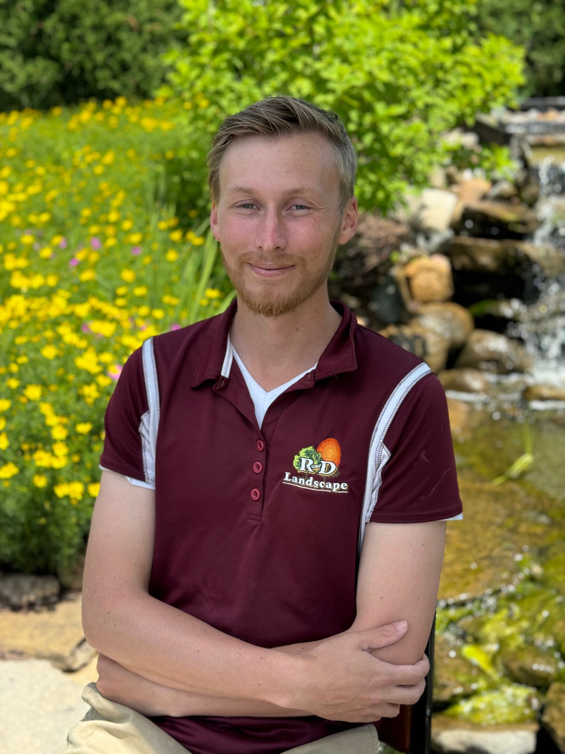 A man in a maroon shirt is standing in front of a waterfall.