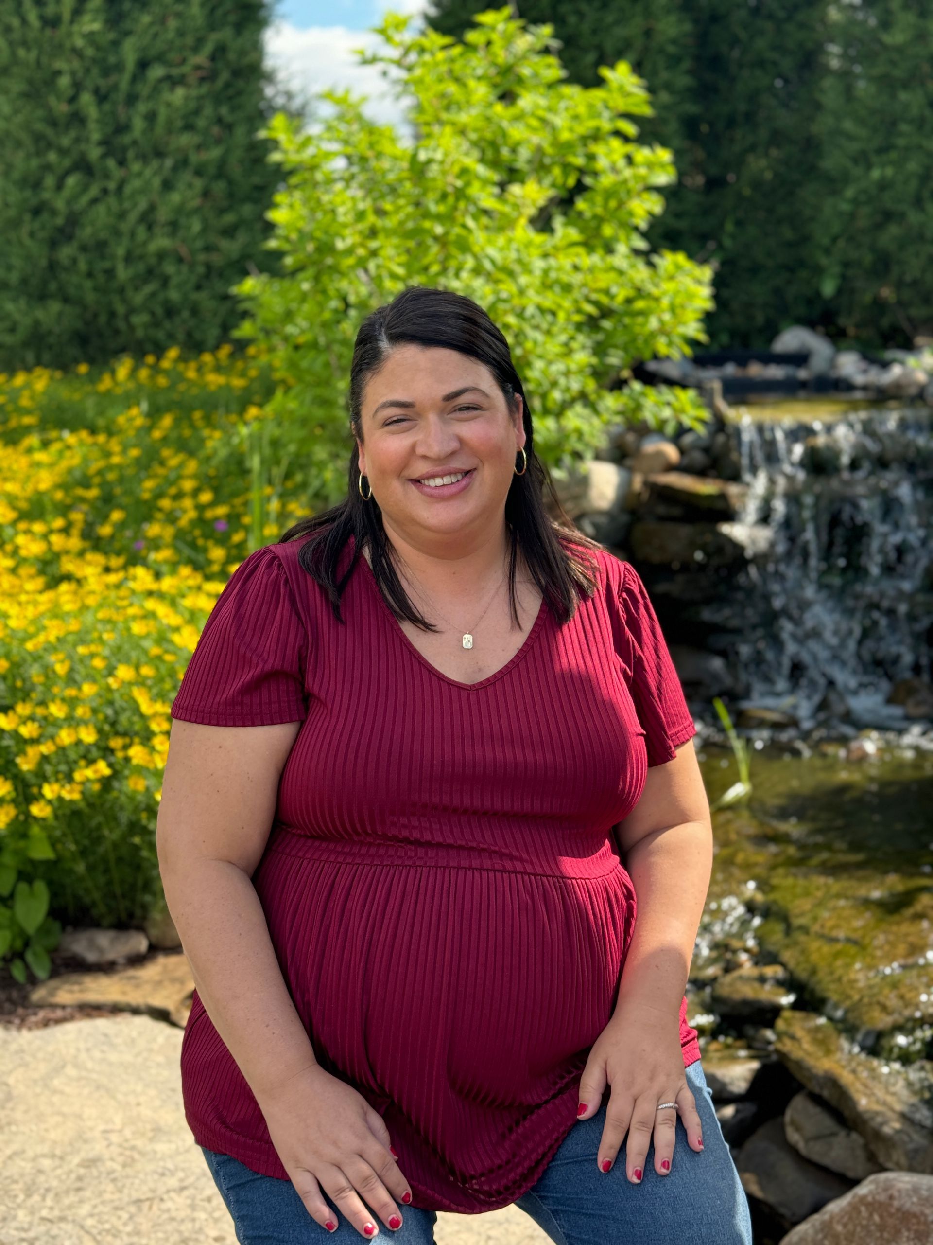 A woman in a red shirt is standing in front of a waterfall.