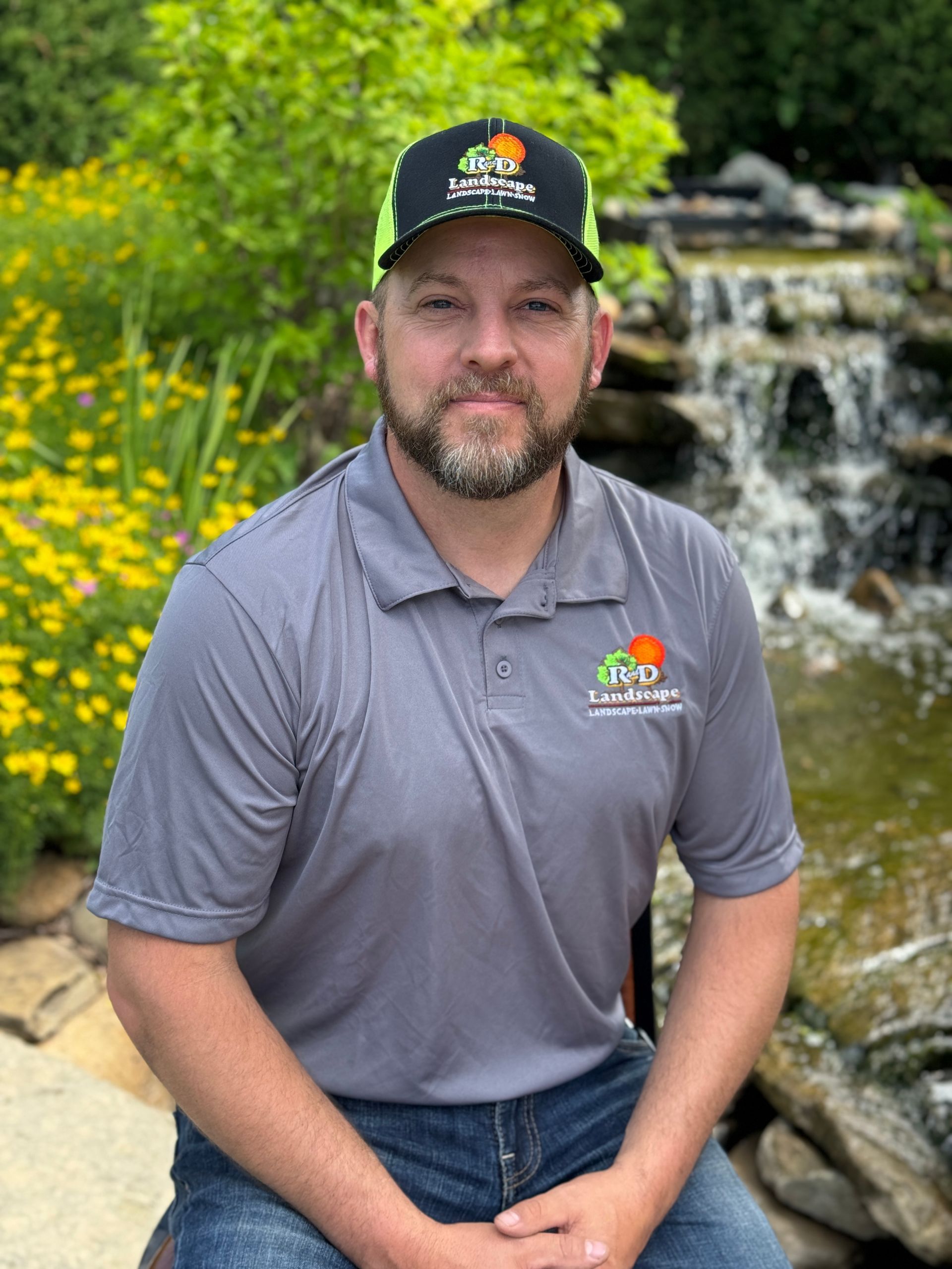 A man wearing a hat and a polo shirt is sitting in front of a waterfall.