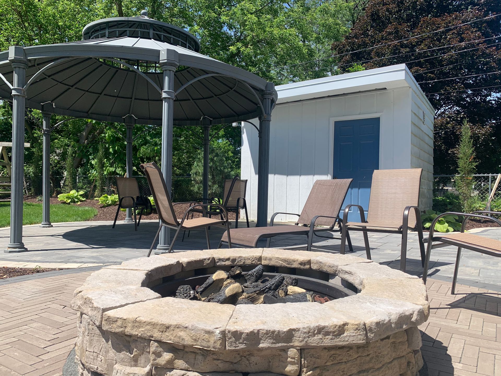 A fire pit with chairs and a gazebo in the background.