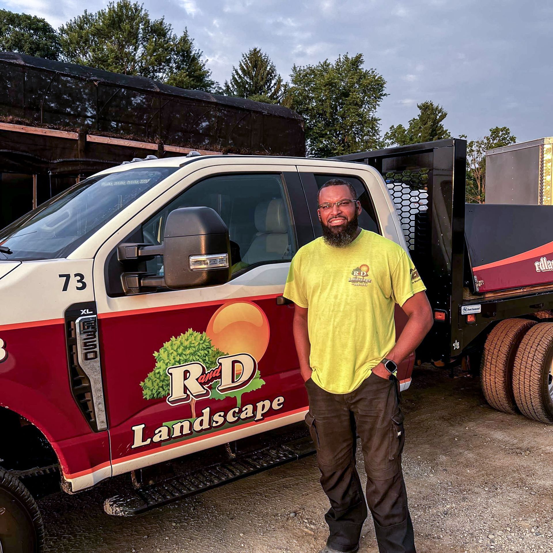 Landscape worker standing beside a red and white RD Landscape truck in a yard
