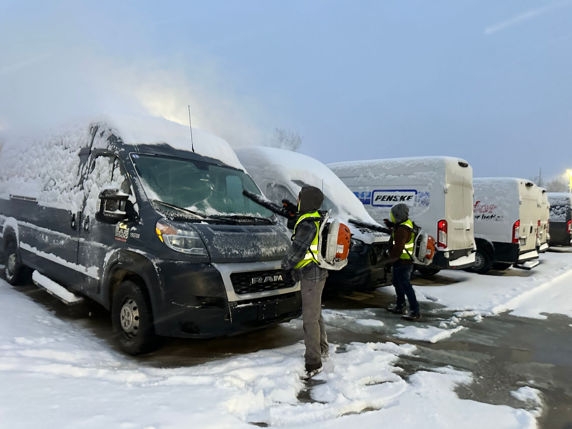 Workers clearing snow off FedEx vans in a snowy parking lot