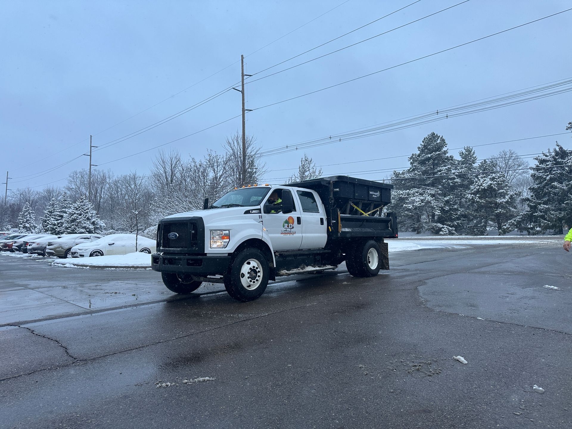 White work truck on a snowy road, with a black dump bed and utility poles in the background.