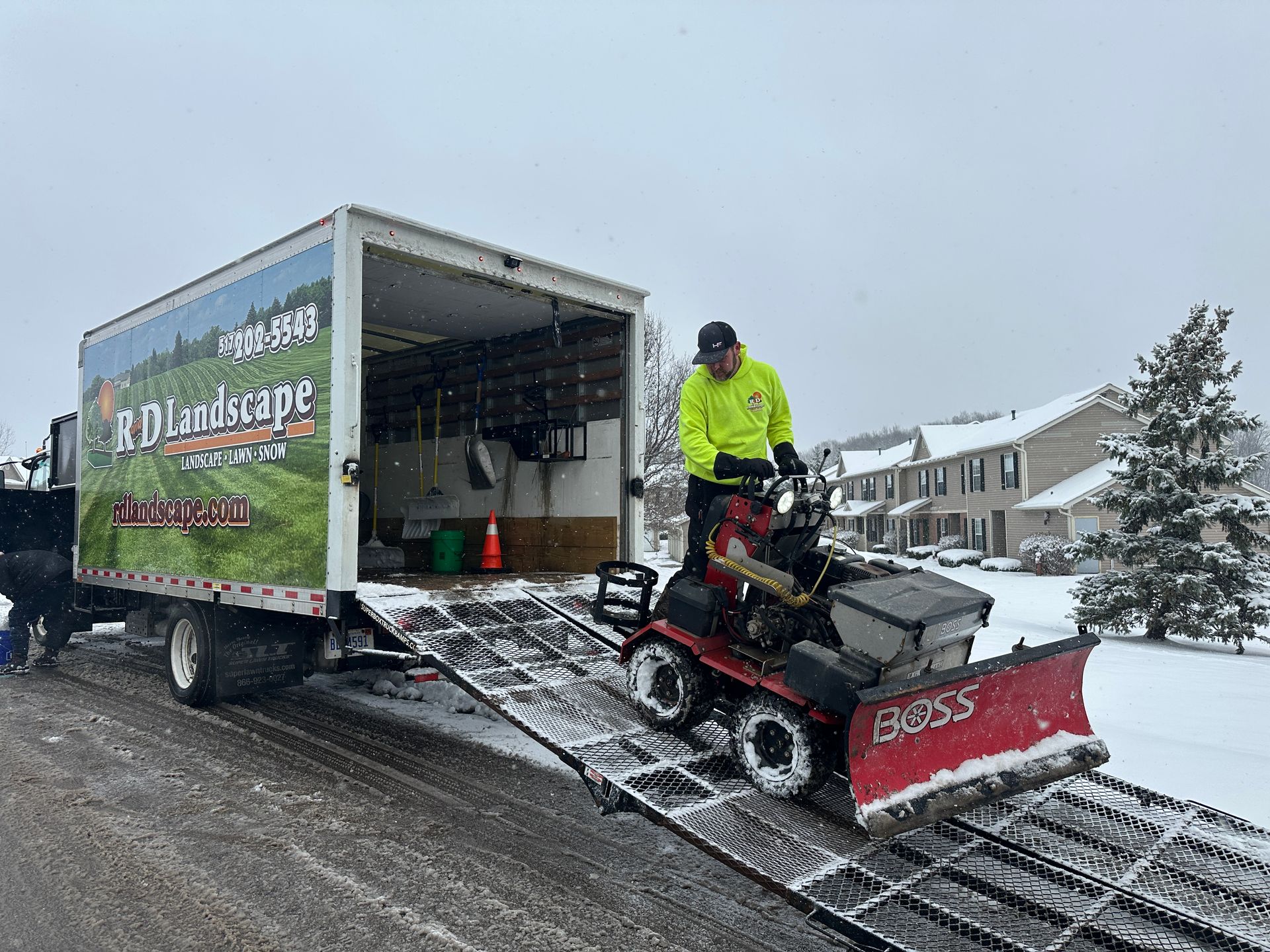 Snowplow unloading equipment from a large truck on a snowy street.