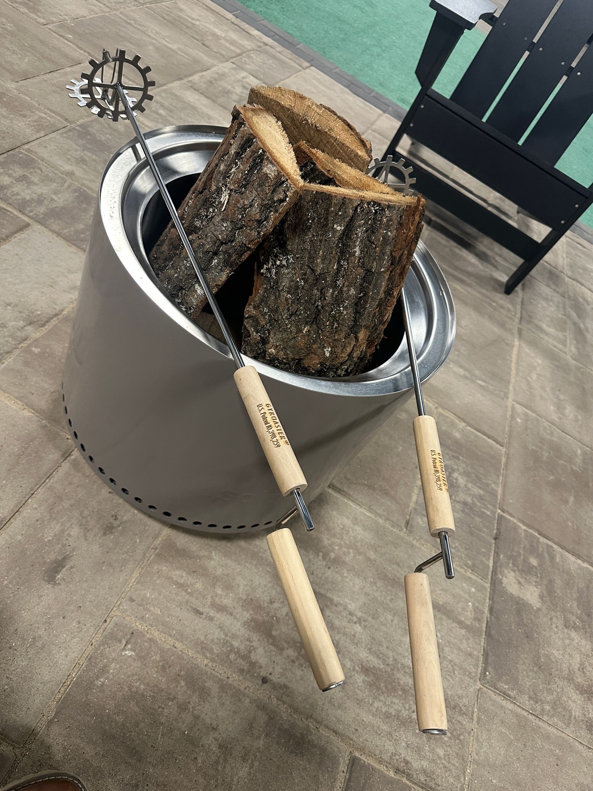 A fire pit filled with logs and tongs on a patio.