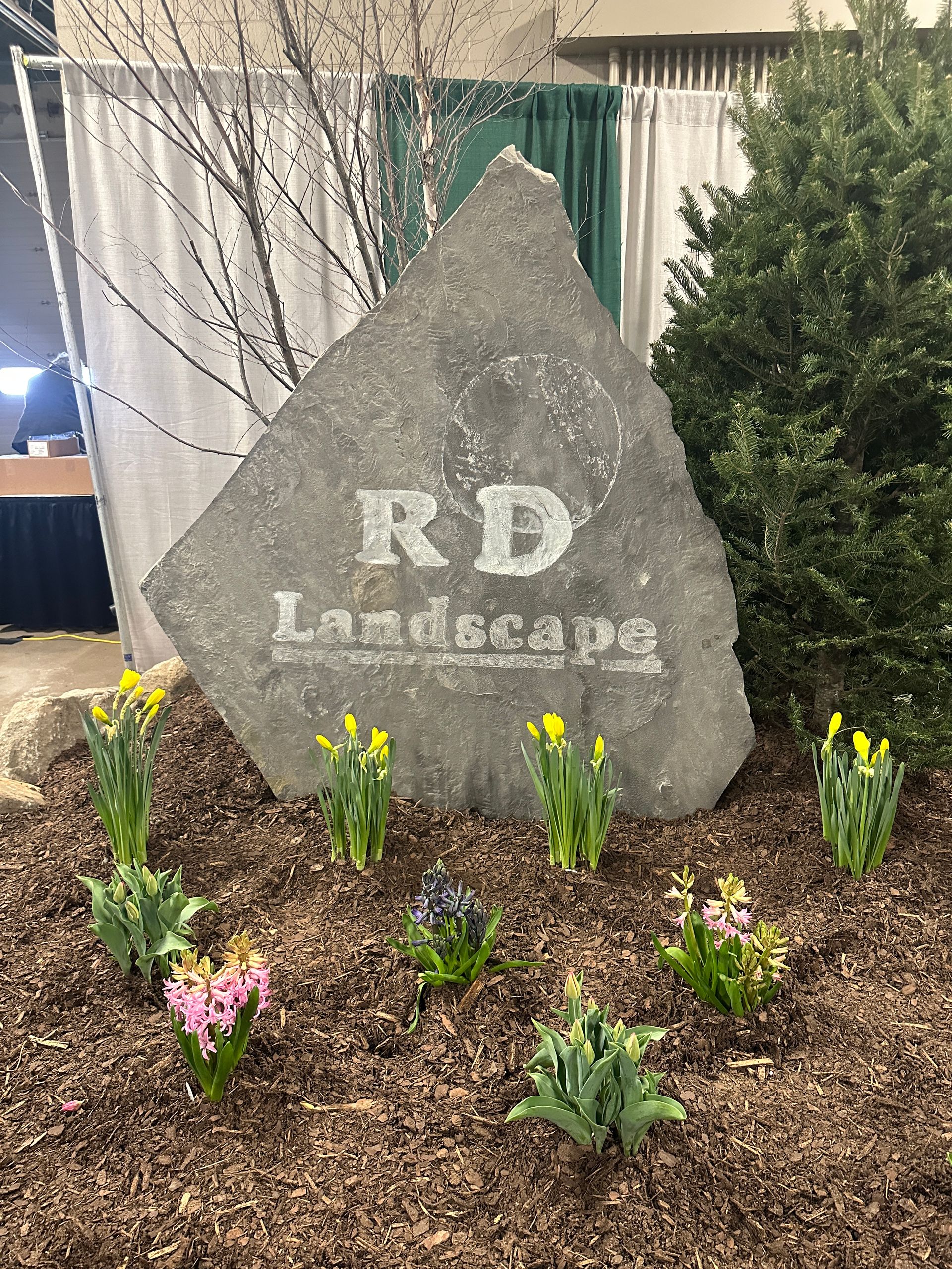 A large rock with the words `` rd landscape '' written on it is surrounded by flowers.