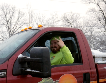 Man in a red pickup truck waving from the driver’s seat, wearing a neon green sweatshirt.
