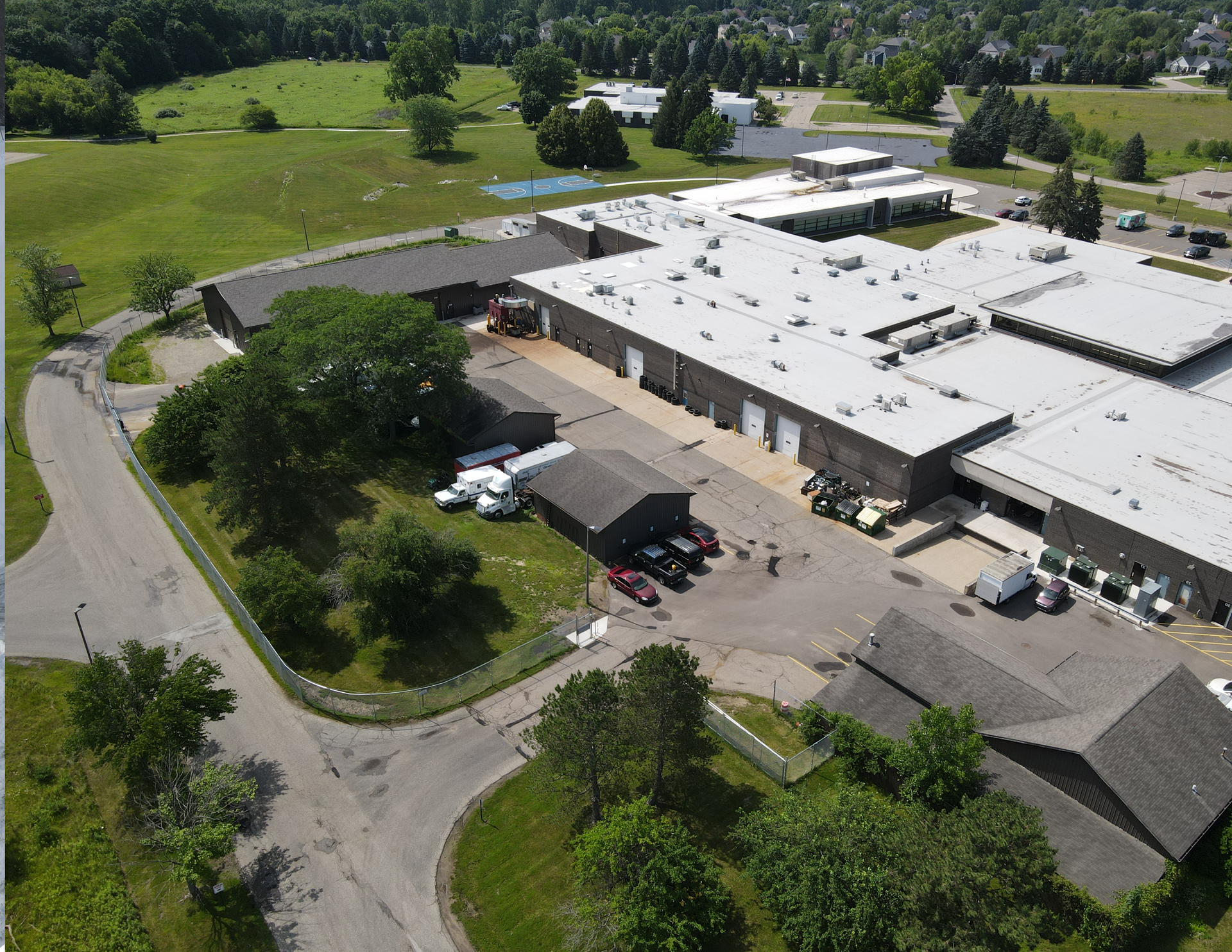 Aerial view of a large industrial building with parking lots, trees, and curving access roads.