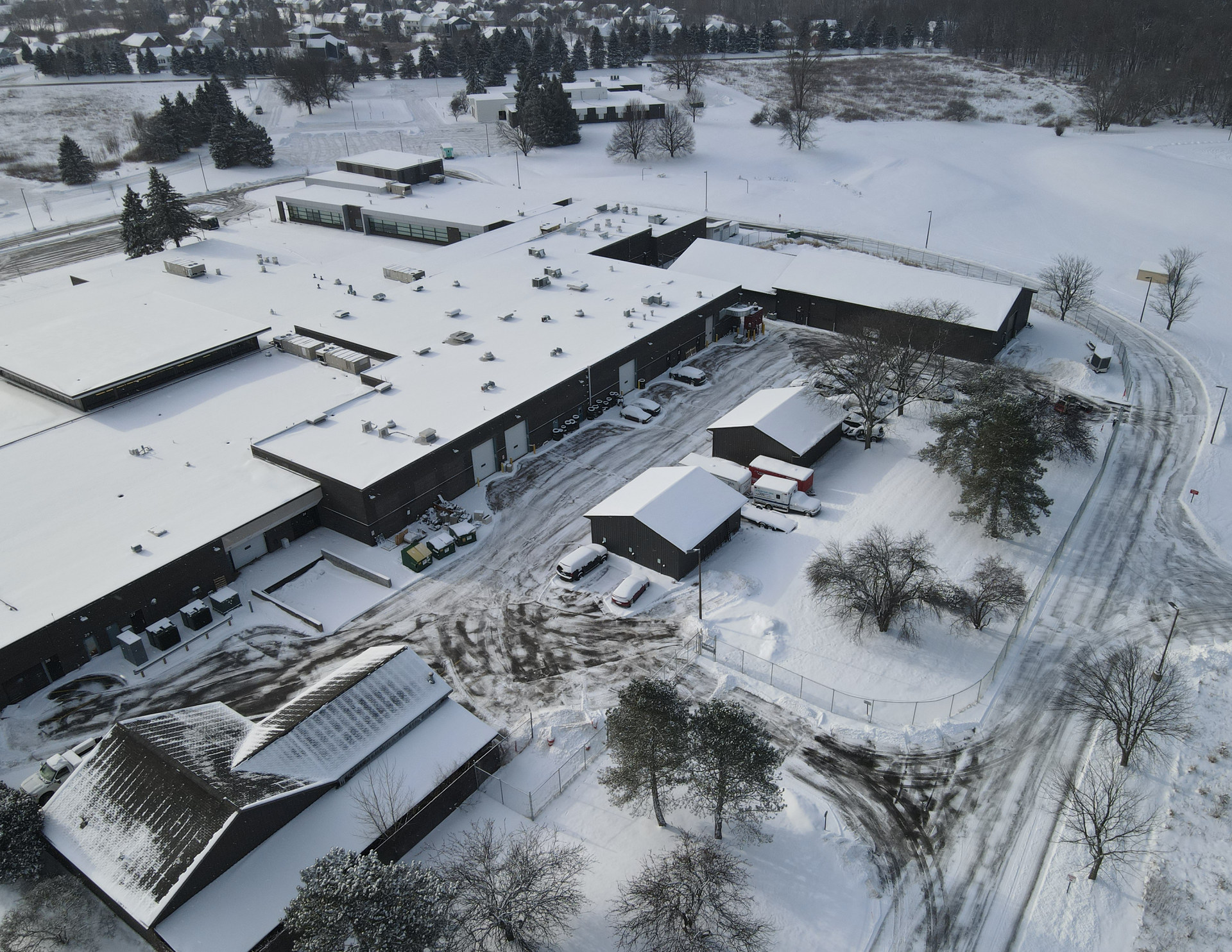 Snow-covered aerial view of a large building complex and surrounding roads in winter